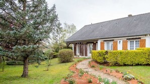 Una casa amb un camí de jardí que condueix a l'entrada, envoltada de verdura i un arbre gran.