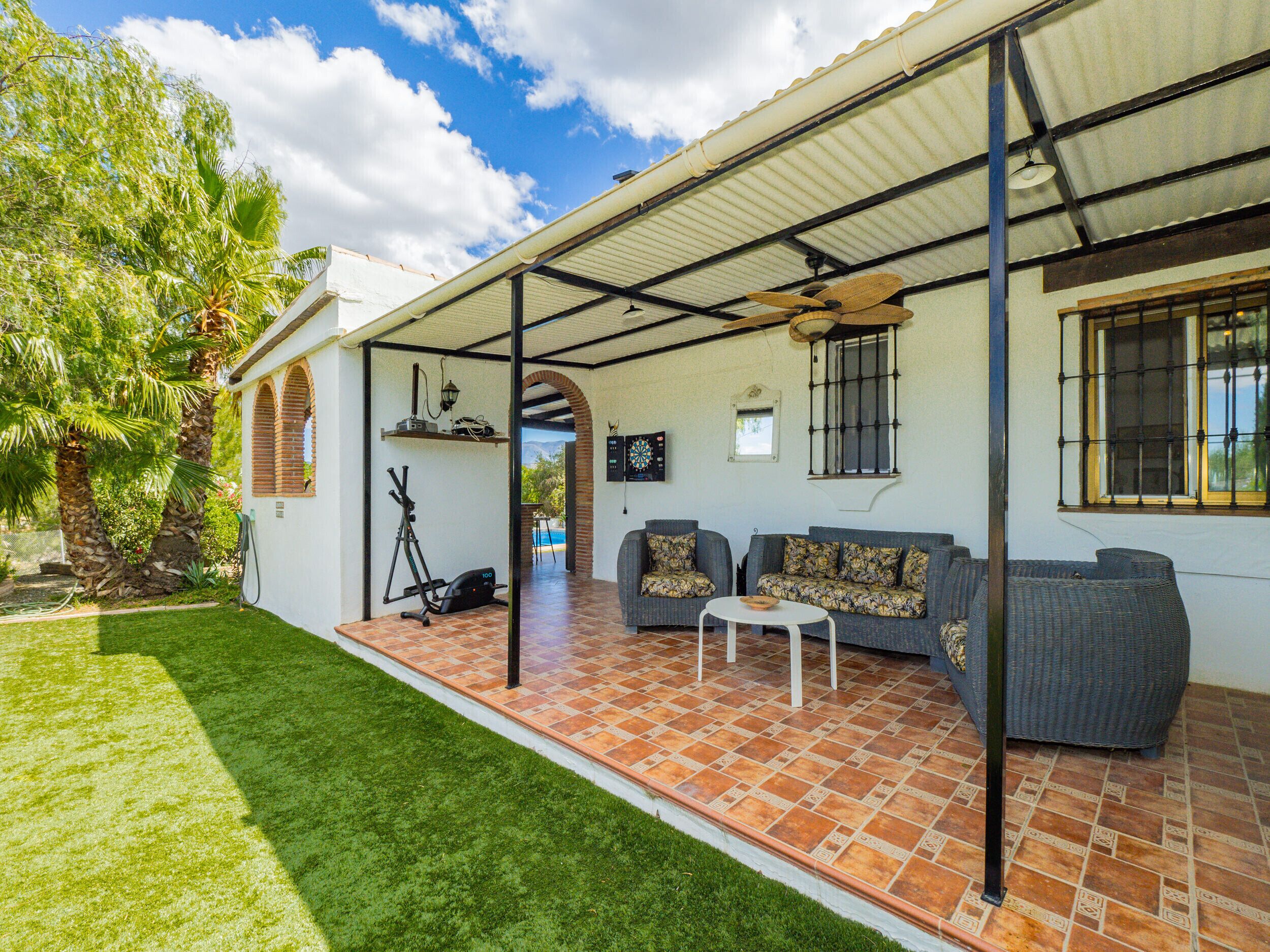 Eine überdachte Terrasse mit Gartenmöbeln, Deckenventilator und Blick ins Grüne.