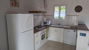 Cozinha compacta com eletrodomésticos brancos, uma janela e um relógio na parede.