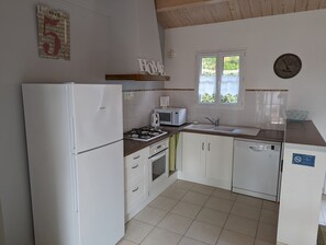 Et lille køkken med hvide hårde hvidevarer, et vindue og et ur på væggen.