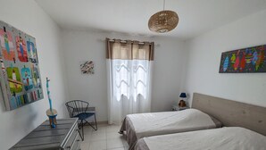 Quarto com duas camas, uma escrivaninha, uma cadeira, um guarda-roupa, uma janela com cortinas e um lustre.