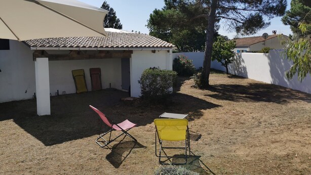 Uma casa com telhado de telhas, varanda coberta e pequeno jardim com duas cadeiras e uma mesa.