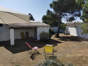 A covered outdoor area with a white building, a red folding chair, a yellow folding chair, and a large tree.
