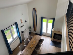 Een eethoek met een houten tafel en stoelen, een surfboard aan de muur en uitzicht op het buitenleven door een raam.
