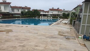 Une piscine avec une terrasse carrelée, des chaises longues et un enrouleur de tuyau d’arrosage.
