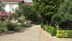 Un sentier pavé de pierres menant à un bâtiment surmonté d’un toit de tuiles rouges, entouré d’une végétation luxuriante et de plantes en fleurs.