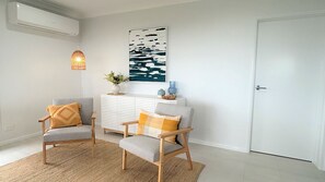 Un salon moderne avec deux fauteuils gris, un radiateur blanc, une œuvre d’art accrochée au mur et une porte.