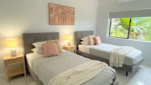 Un dormitorio con dos camas, mesitas de noche, una obra de arte en la pared y una ventana con vistas a la vegetación.