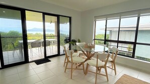 A dining area with a glass table and chairs, large windows, and a view of greenery and mountains.