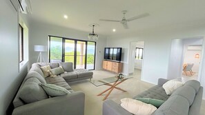 Een moderne woonkamer met een hoekbank, een glazen salontafel, een televisie en een balkon met uitzicht.