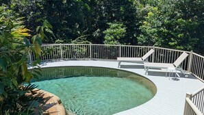 A swimming pool with a curved deck, surrounded by a white railing, and shaded by trees.