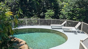 Una piscina con un borde curvo, rodeada por una barandilla blanca y con sombra de árboles.