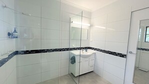 A modern bathroom with white tiles, a glass shower enclosure, and a white sink with a black tile accent.