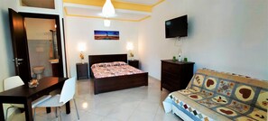 A bedroom with a bed, a TV, a sofa, a desk, and a chair.