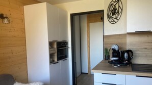 A compact kitchen with built-in appliances, a coffee maker, and a kettle on the counter.