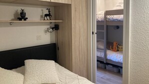 A bedroom with a bunk bed, a bedside table, a wall-mounted shelf with decorative items, and a power outlet.