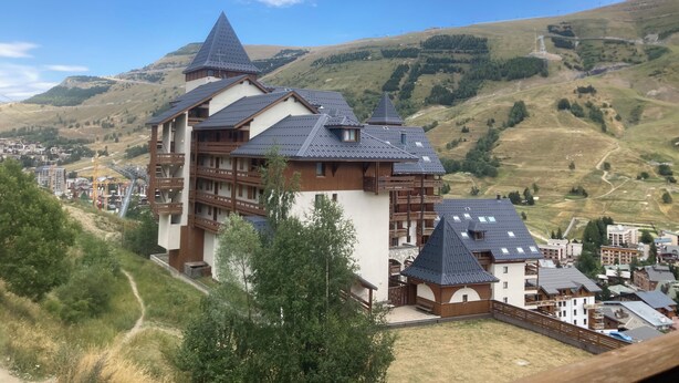 A multi-story hotel with a prominent tower, set against a backdrop of rolling hills and a clear sky.