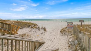 Ein Strand mit einer Holzpromenade, die zum Ufer führt, einem Warnschild und einem klaren Himmel.