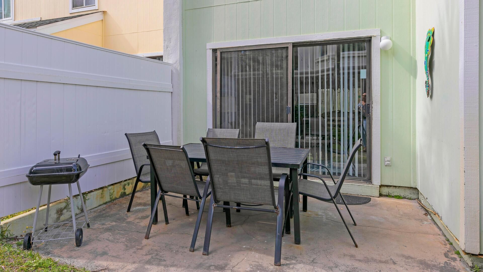 En udendørs terrasse med et bord, stole, grill og en skydedør.