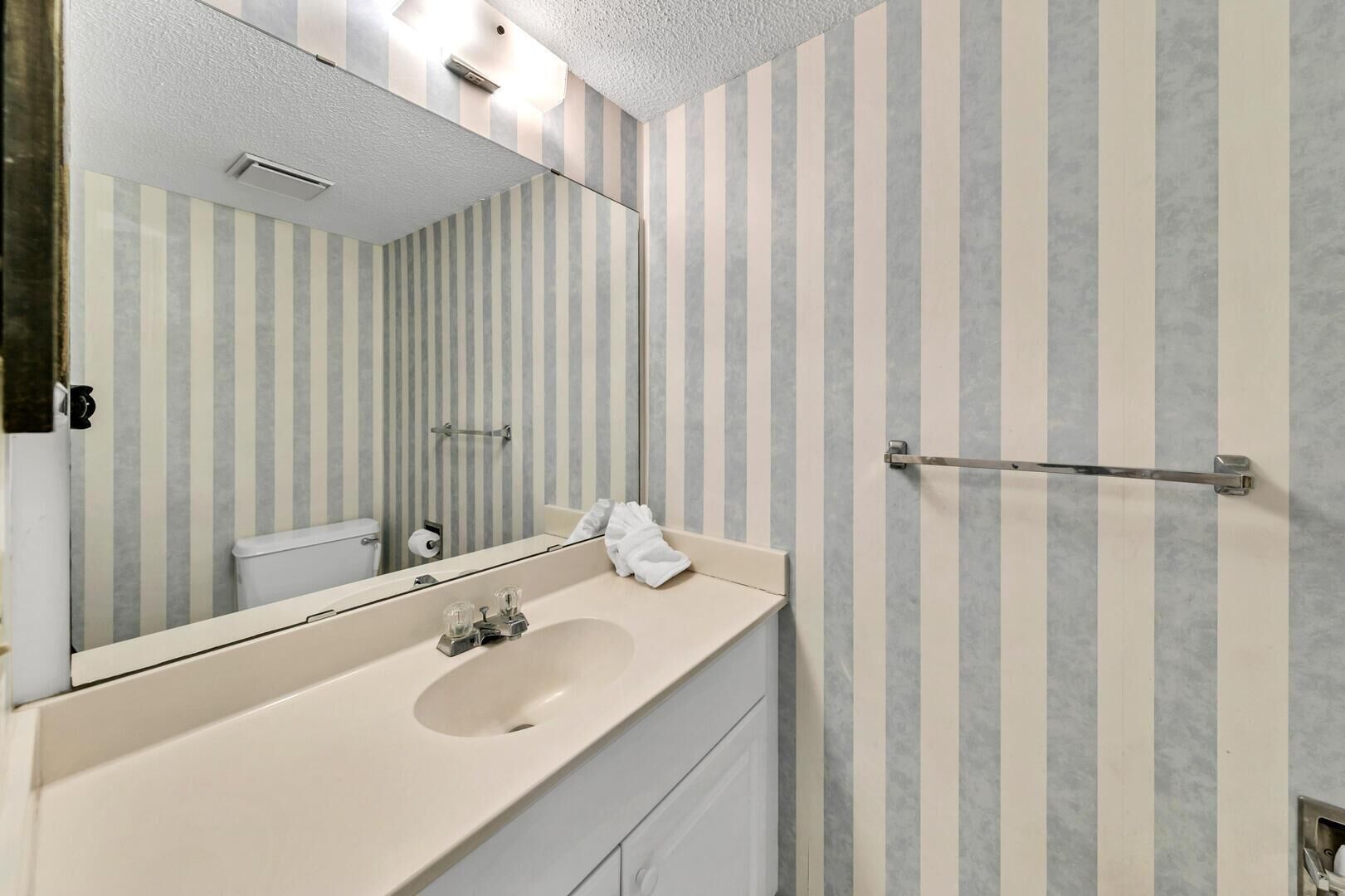 A bathroom with a striped wall, a sink with a mirror, and a towel rack.