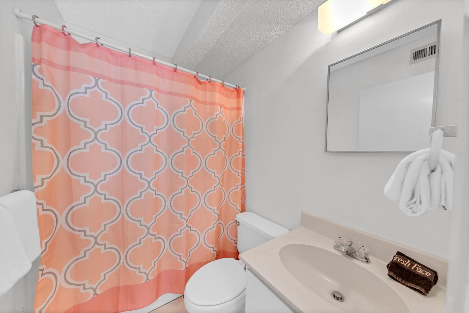 A bathroom with a patterned shower curtain, a white toilet, a sink with a towel, and a mirror.