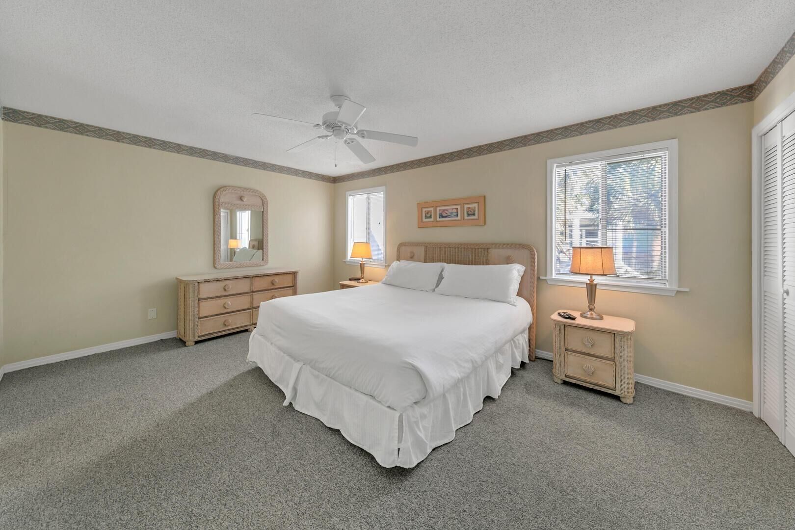 A bedroom with a bed, two nightstands, a ceiling fan, a dresser, and a window with blinds.