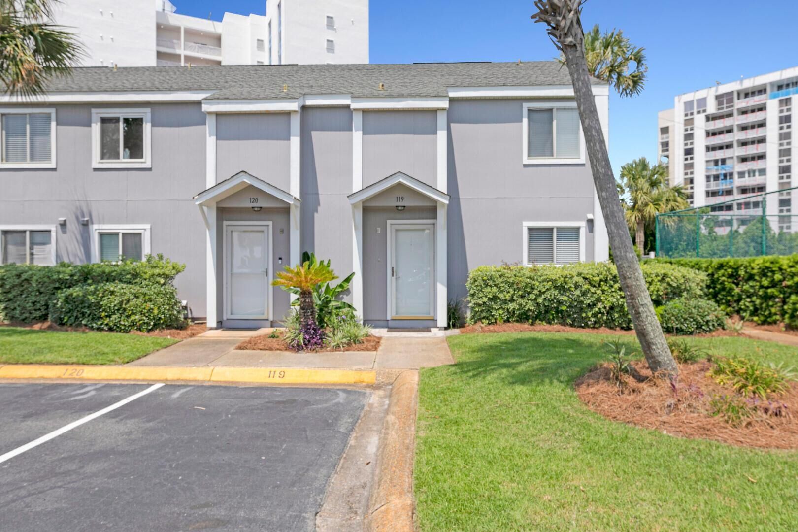 A two-story building with numbered doors, a parking lot, and a well-maintained lawn with a palm tree.