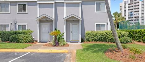 A two-story building with numbered doors, a parking lot, and a well-maintained lawn with a palm tree.