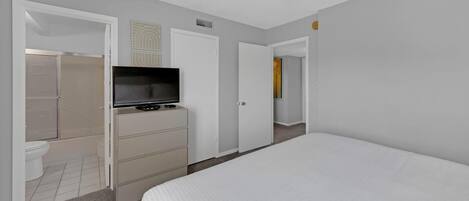 A hotel room with a bed, a TV on a dresser, a shower, and a door leading to another room.