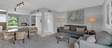 A modern living room with a glass dining table, grey sofas, and a coffee table.
