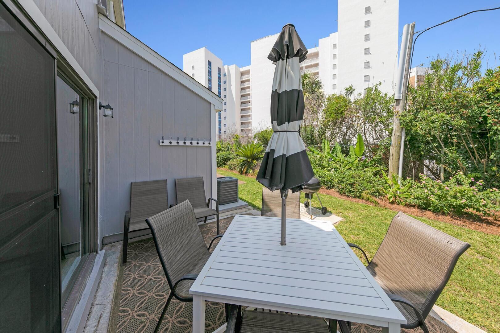 Un patio al aire libre con una mesa, sillas, una sombrilla y una parrilla.