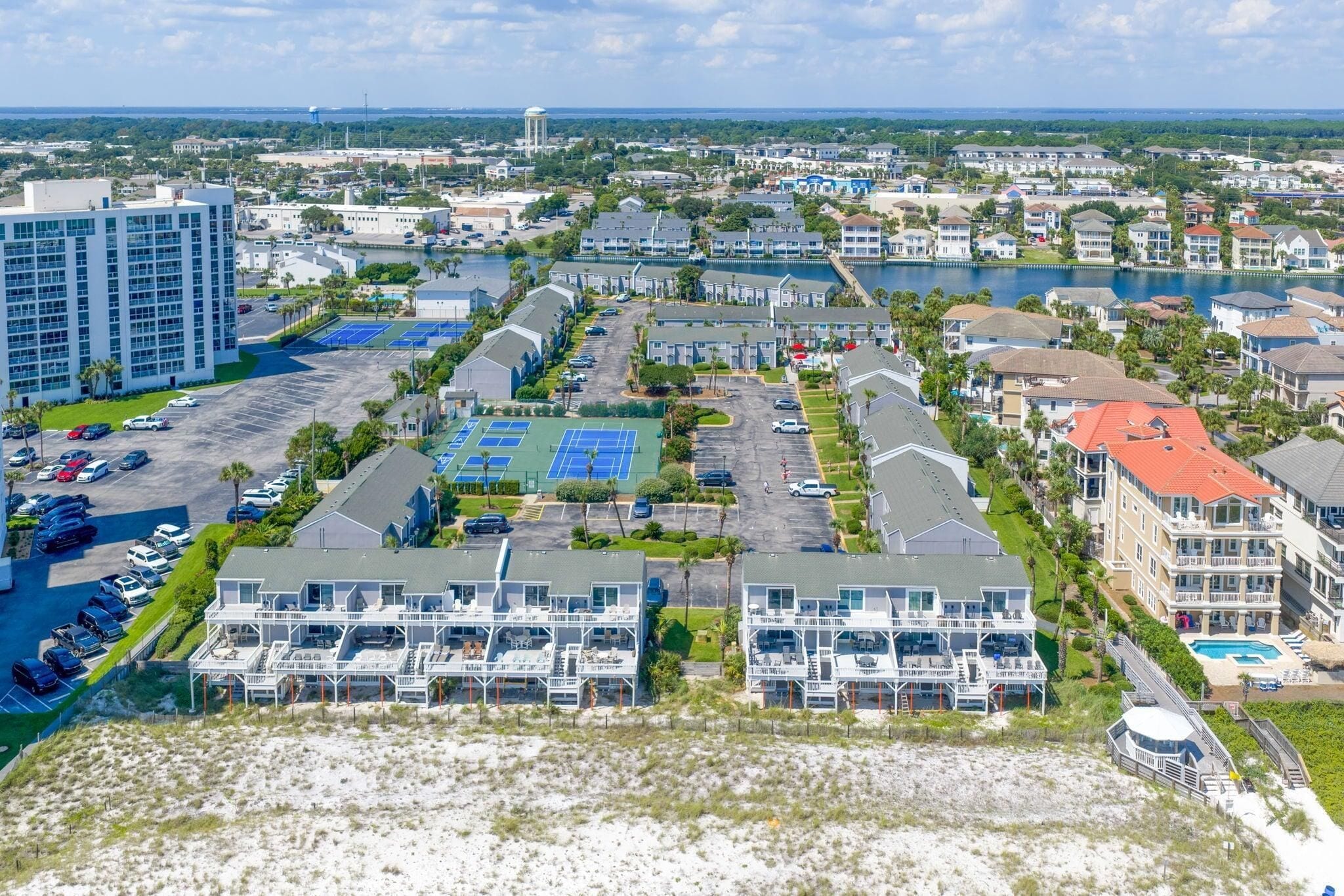 A coastal hotel with multiple-story buildings, a tennis court, and a beach area.