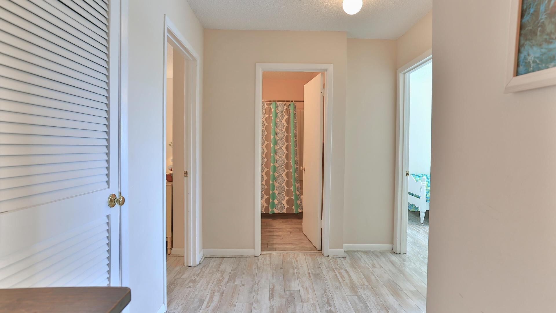A hallway with a wooden floor, a door with a brass handle, and a patterned curtain.
