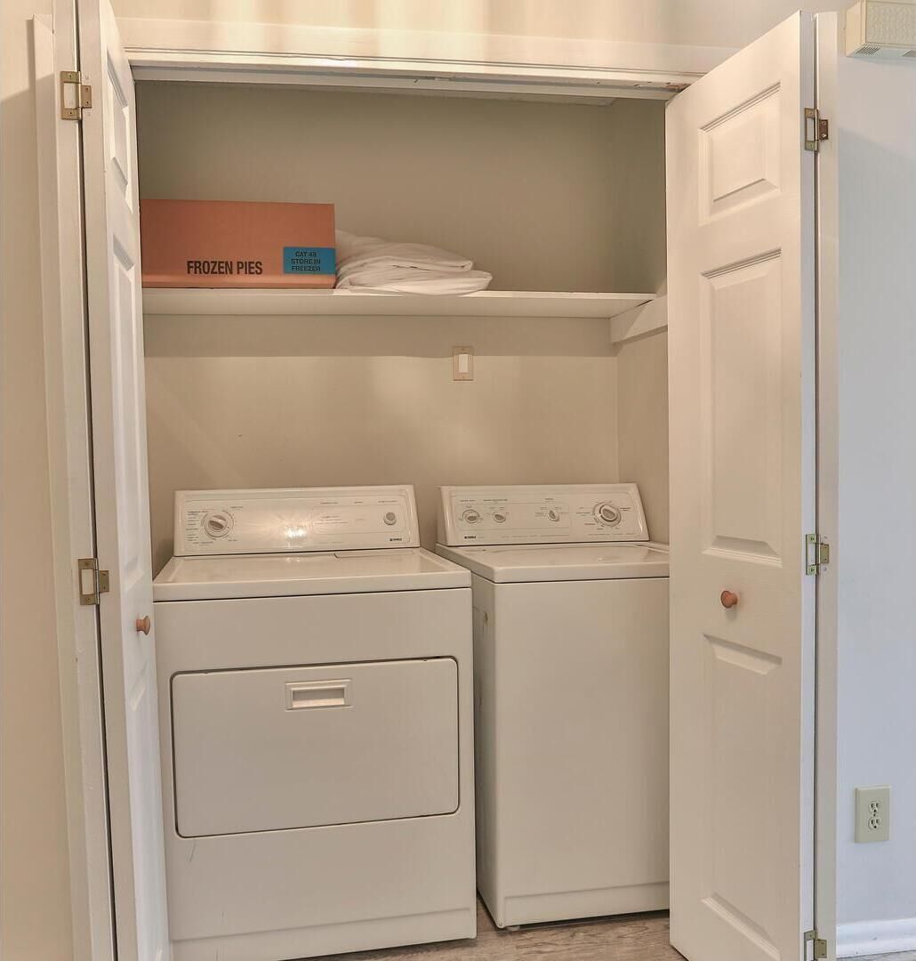 A laundry room with two front-loading washers and a shelf above containing a box labeled "FROZEN PIES".