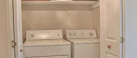 A laundry room with two front-loading washers and a shelf above containing a box labeled "FROZEN PIES".