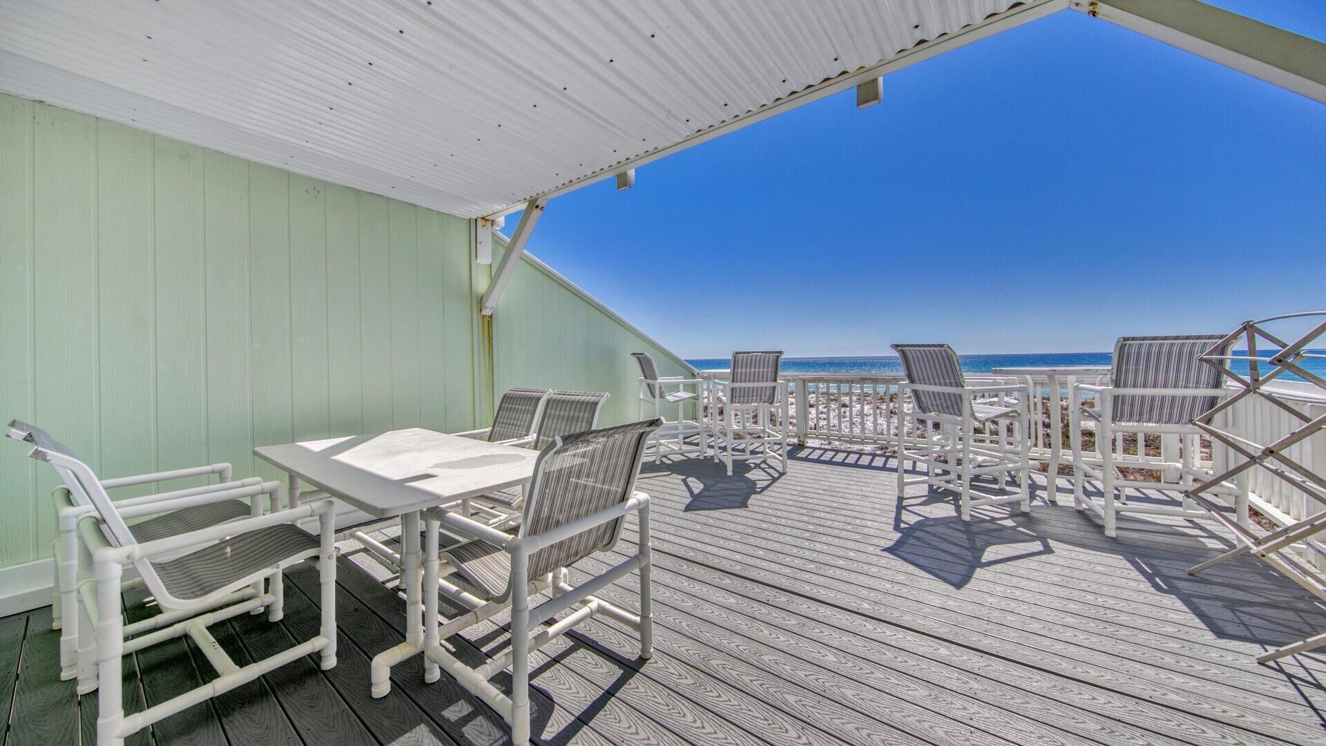 A covered outdoor seating area with a table and chairs, overlooking a beach.