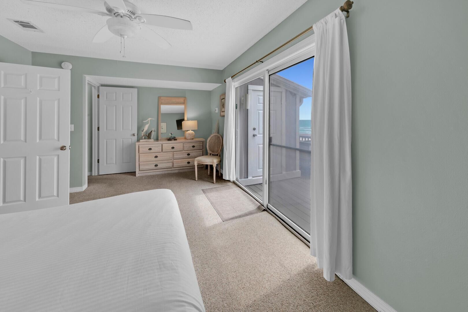 A bedroom with a bed, a dresser, a chair, and a sliding glass door leading to a balcony.