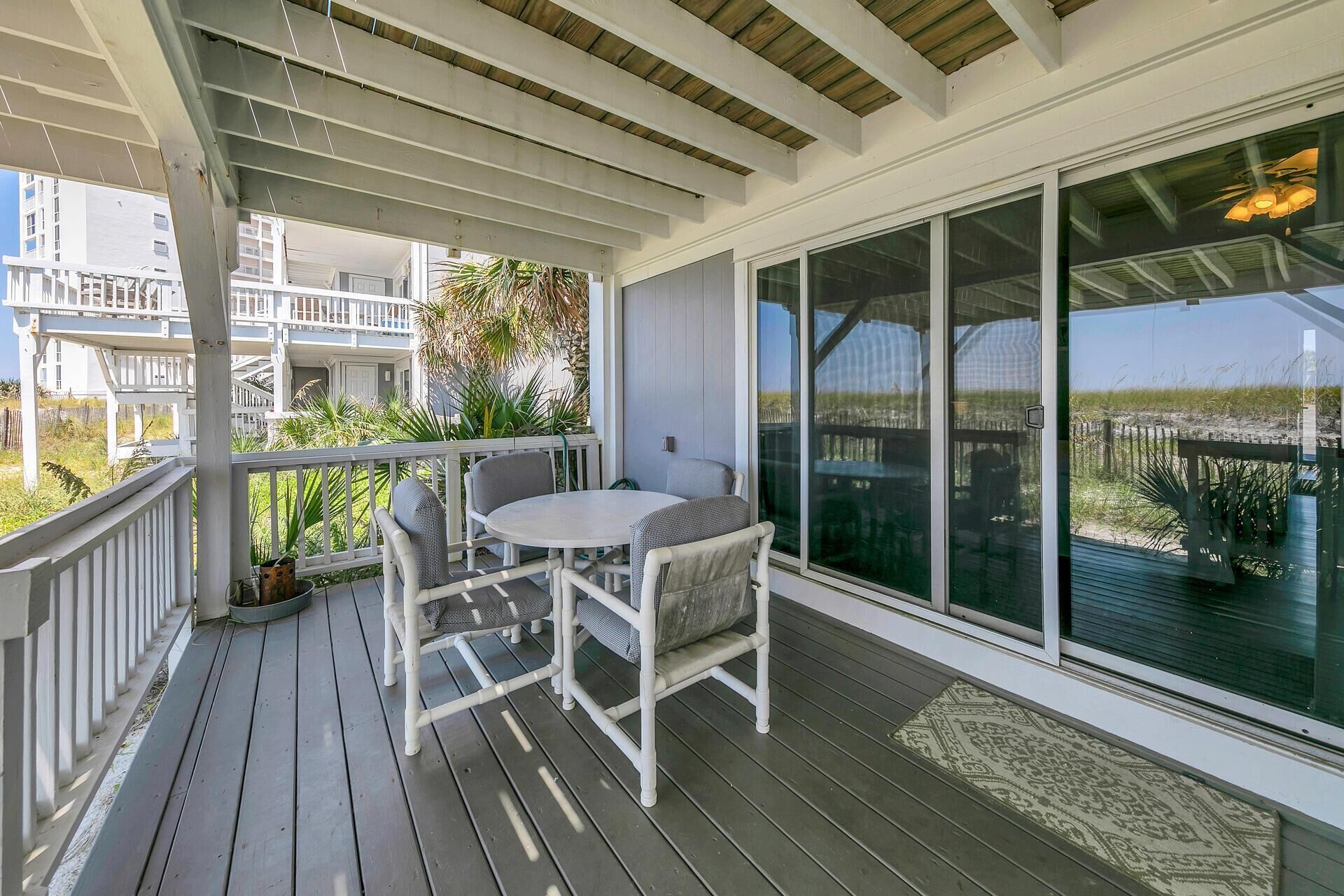A covered outdoor area with a table and chairs, large sliding glass doors, and a view of a building and vegetation.