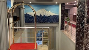 A hotel lobby with a red carpet, a mural of a mountain, a gold elevator, and marble walls.