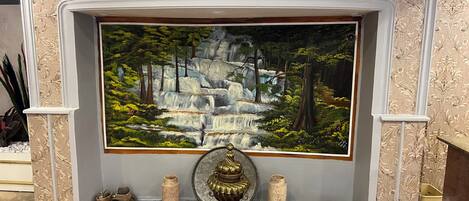 A fireplace with a painting of a waterfall, surrounded by decorative vases and a sculpture.