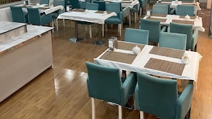A spacious dining area with teal chairs and white tables, featuring a large mural on the wall and a modern ceiling design.