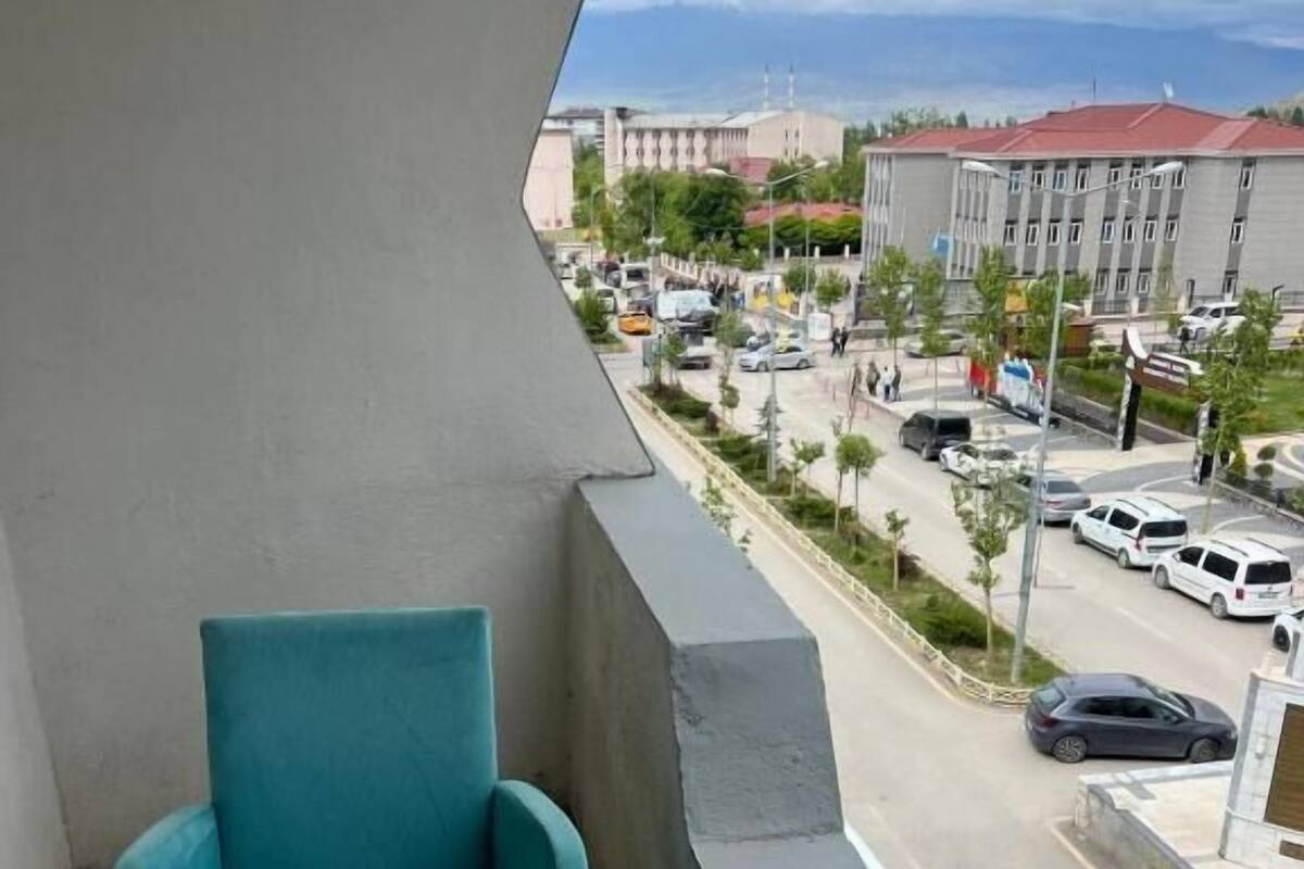 A balcony with a teal chair and a small white table, overlooking a parking lot and buildings.