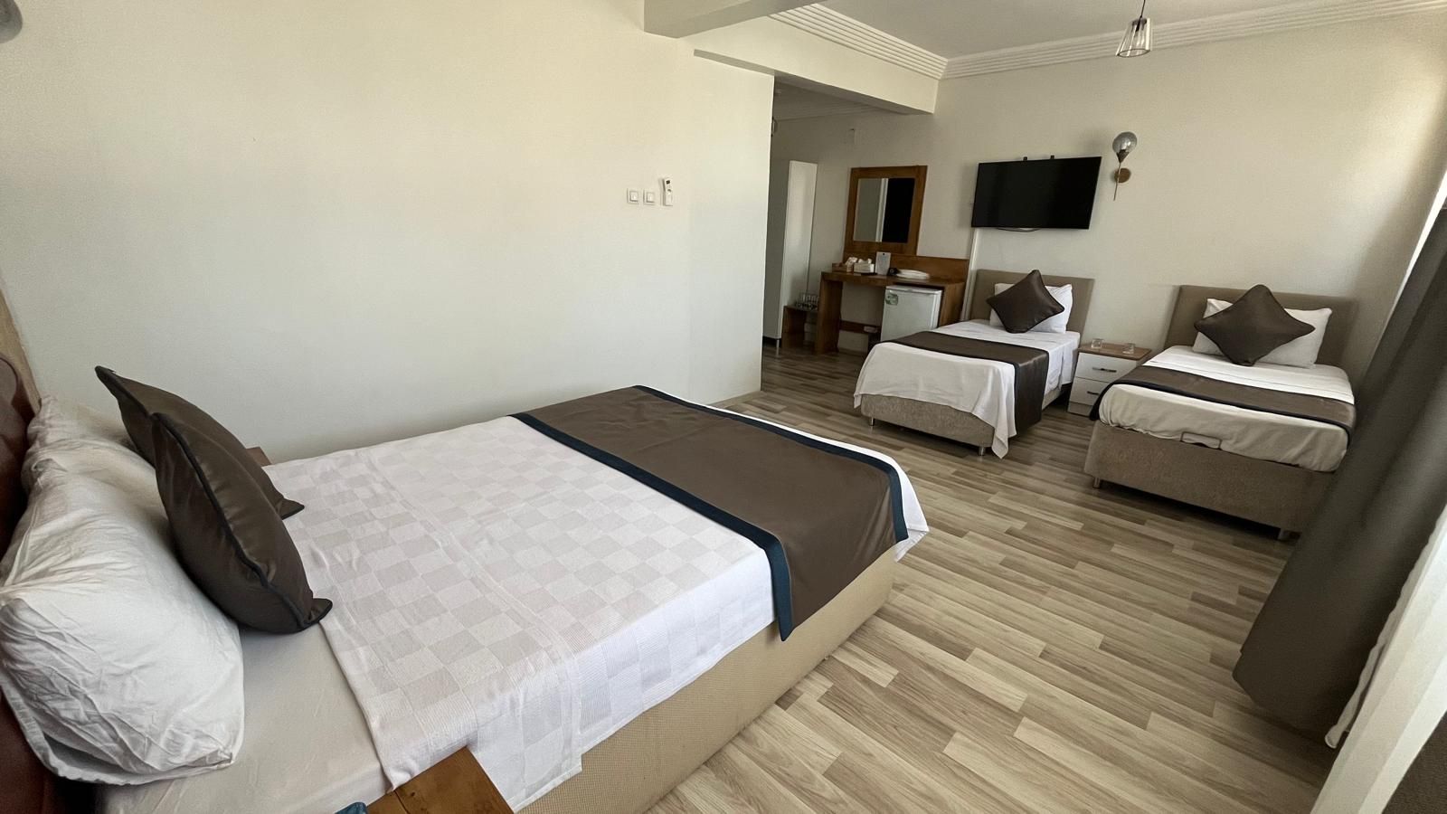 A hotel room with a large bed, two smaller beds, a desk, and a TV.