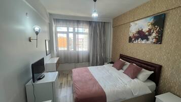 Un dormitorio con cama, escritorio, silla, lámpara y ventana con cortinas.