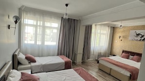 A hotel room with three beds, a large window with curtains, a wooden floor, and a wall-mounted light fixture.