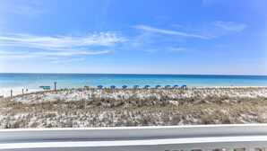 Blick auf einen Strand mit einer Reihe blauer Sonnenschirme und feinem Sand.