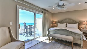Ein Schlafzimmer mit Bett, Sessel, Tisch und Blick auf das Meer durch eine Schiebetür.