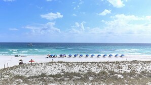 Ein Strand mit weißem Sand, eine Reihe blauer Sonnenschirme und ein Boot im Wasser.