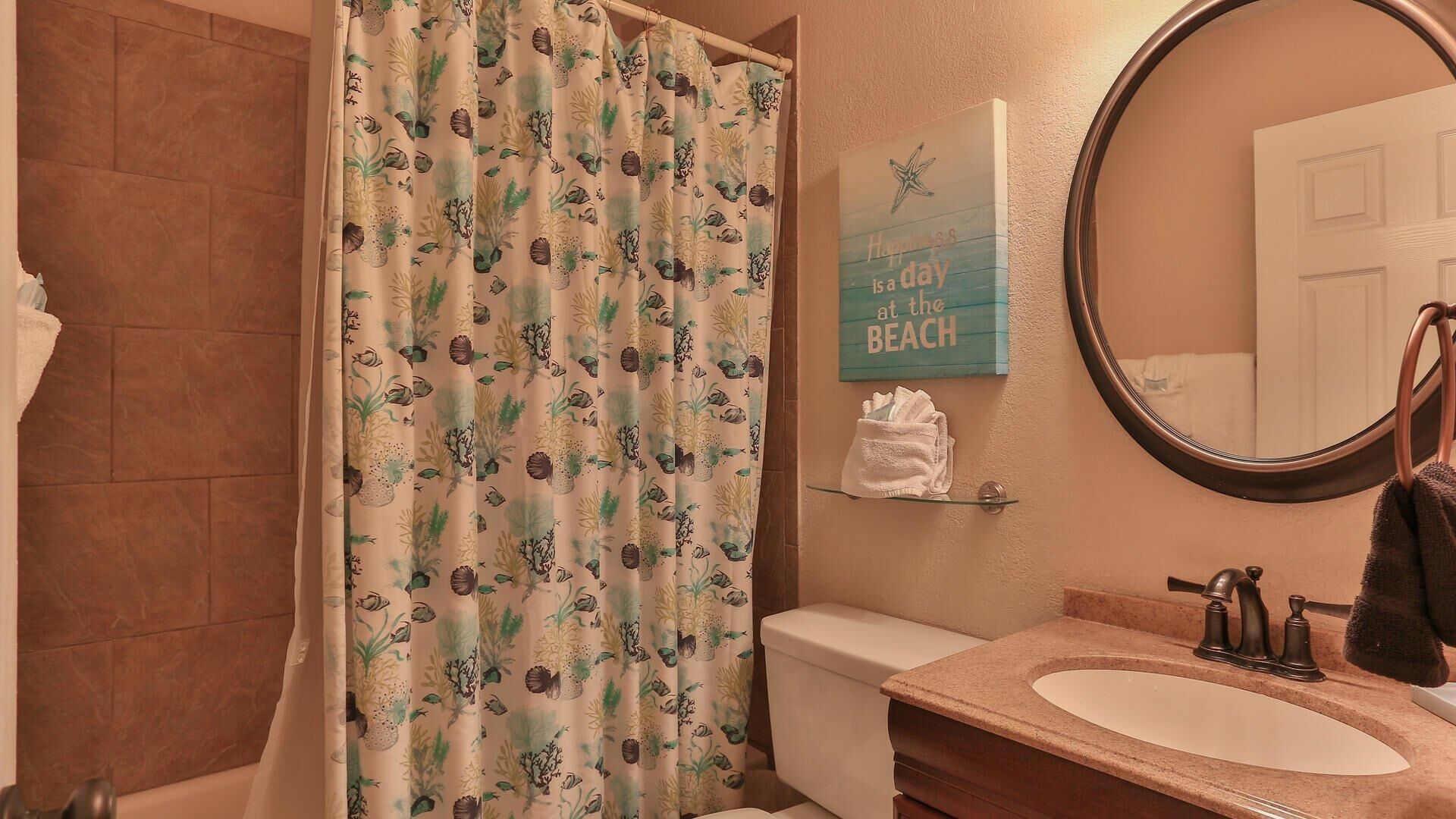 A bathroom with a shower curtain featuring a tropical pattern, a toilet, a sink with a mirror, and a towel rack.