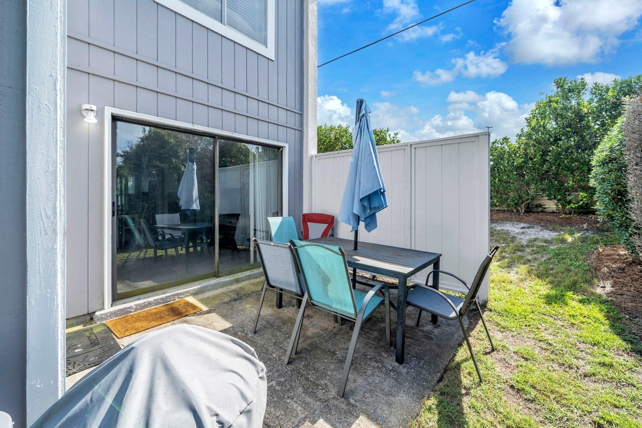 Une terrasse avec une table et des chaises, un parasol et une porte-fenêtre coulissante donnant sur un espace intérieur.